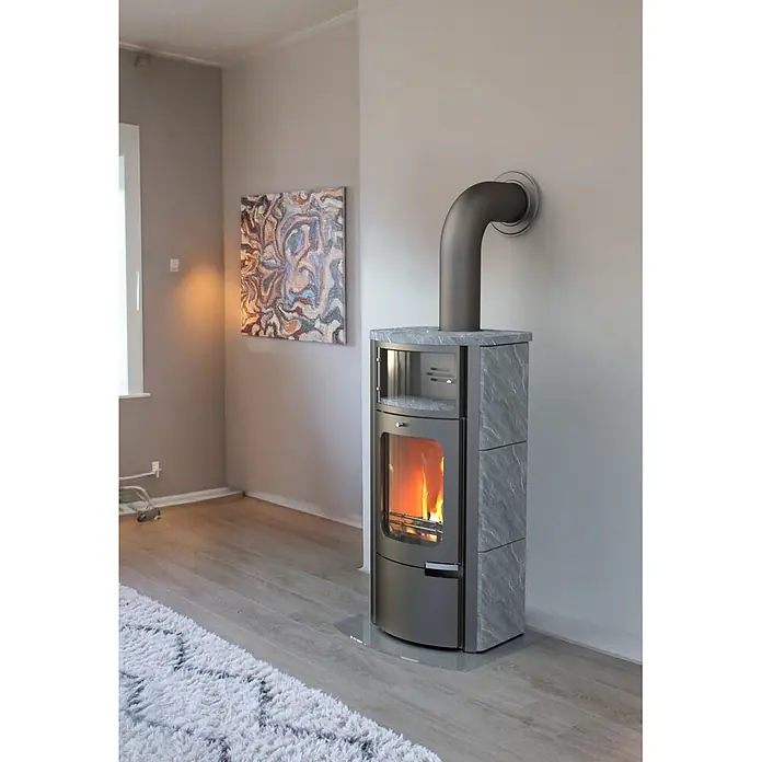 Kaminofen Prestige - 7 kW, Raumheizvermögen: 200 m³, Material Verkleidung: Speckstein - Moderner Kaminofen aus grauem Metall mit Steinverkleidung und sichtbaren Flammen, an einen Wandabzug angeschlossen.