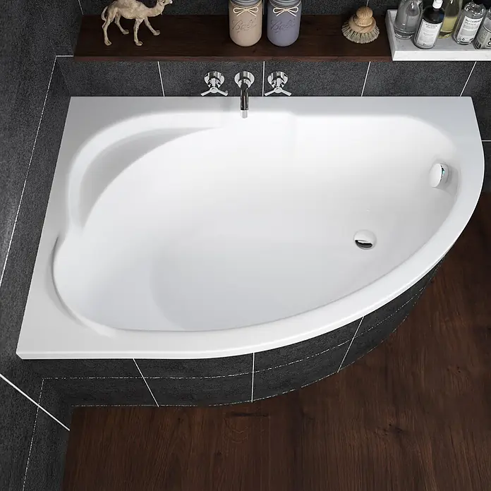 Bad Land Eckbadewanne - L x B: 130 x 85 cm, Sanitäracryl, Weiß - Weiße Eckbadewanne mit Chromarmaturen, in einem Badezimmer mit dunklen Fliesen und dunklem Holzboden.