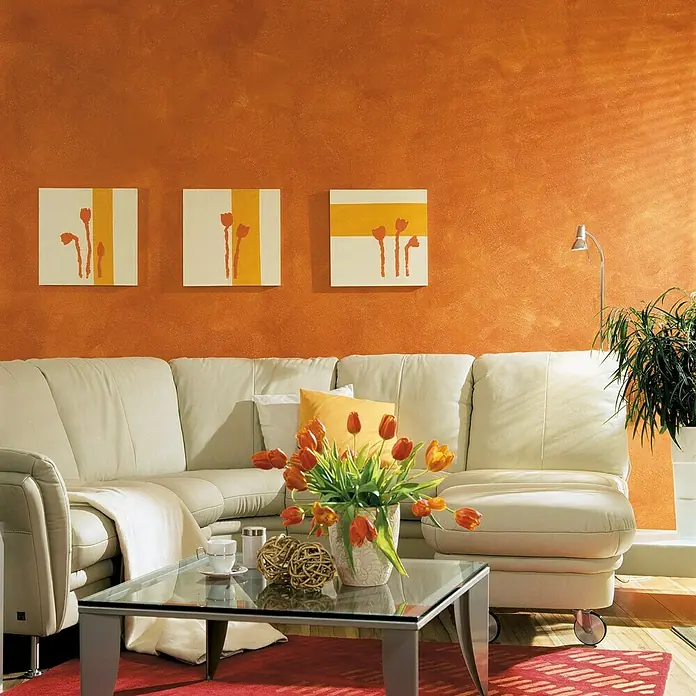 Erfurt Vliestapete Variovlies Flat Classic - Weiß, Uni, 25 x 0,75 m - Wohnzimmer mit cremefarbenem Sofa, Glascouchtisch mit Blumen und orangefarbener Wand mit Kunst.