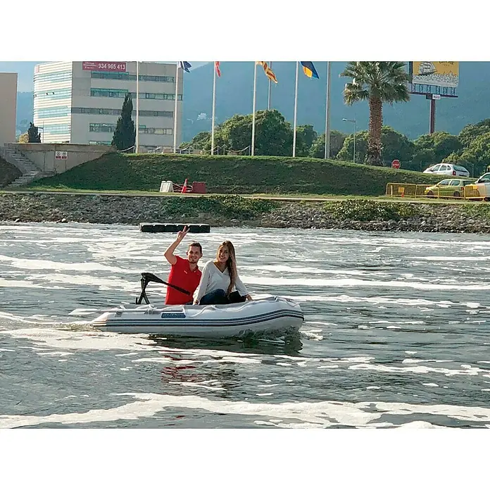 Hidea Motor fueraborda 2,5 HP - 1,8 kW, Control de timón, Eje corto - Una pareja disfruta de un paseo tranquilo en un bote inflable en el agua, rodeado de paisaje urbano y paisaje natural.