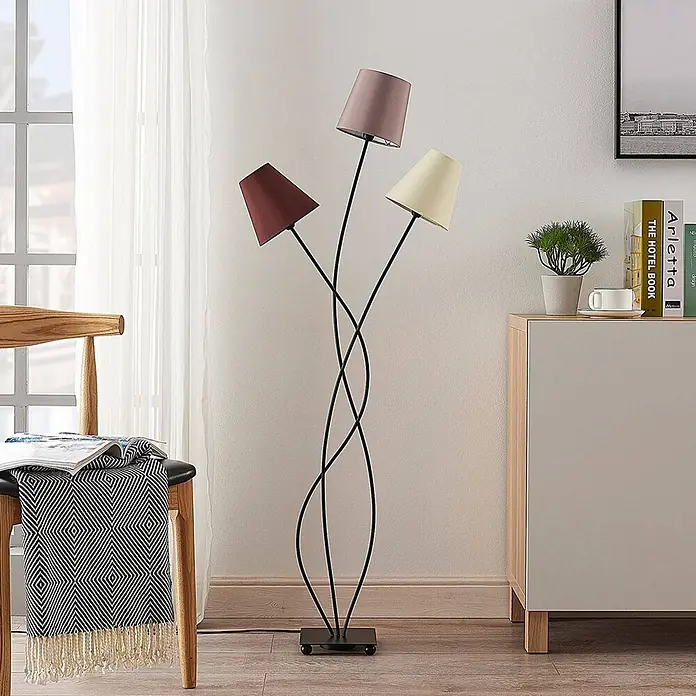 Lindby Stehleuchte Melis - creme / amber, E14 - Stehlampe mit drei geschwungenen schwarzen Metallarmen und mehrfarbigen Stoffschirmen, die einen Wohnraum erhellt.