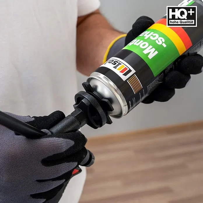 IsolBau Bauschaum 1 x Montageschaum 750 ml - 750 ml - Eine Person in Arbeitshandschuhen befestigt eine grün-gelb-rote Montageschaumdose an einer schwarzen Pistole.