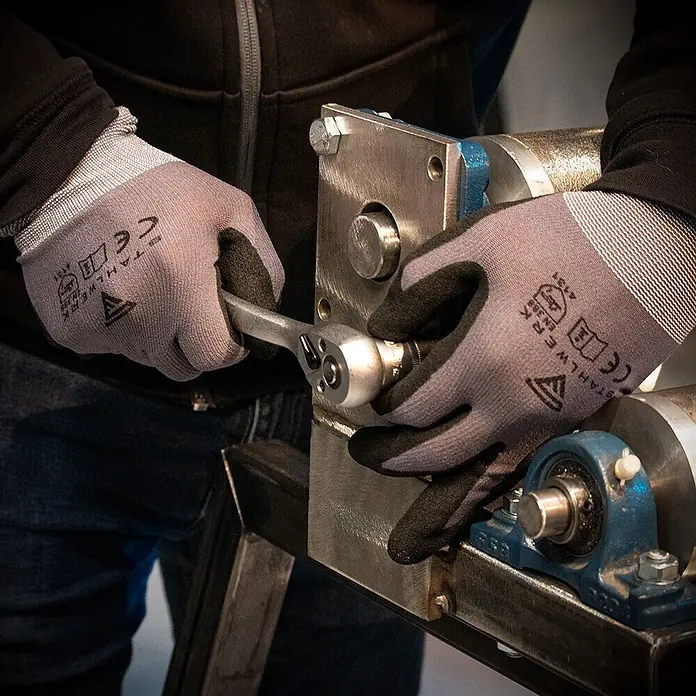 STAHLWERK Arbeitshandschuhe Montagehandschuhe 10 Paar, Größe XL - XL, Grau, Kunststoff, 10 Stk. - Hände in grau-schwarzen Schutzhandschuhen bedienen einen Ratschenschlüssel an einer Maschine.