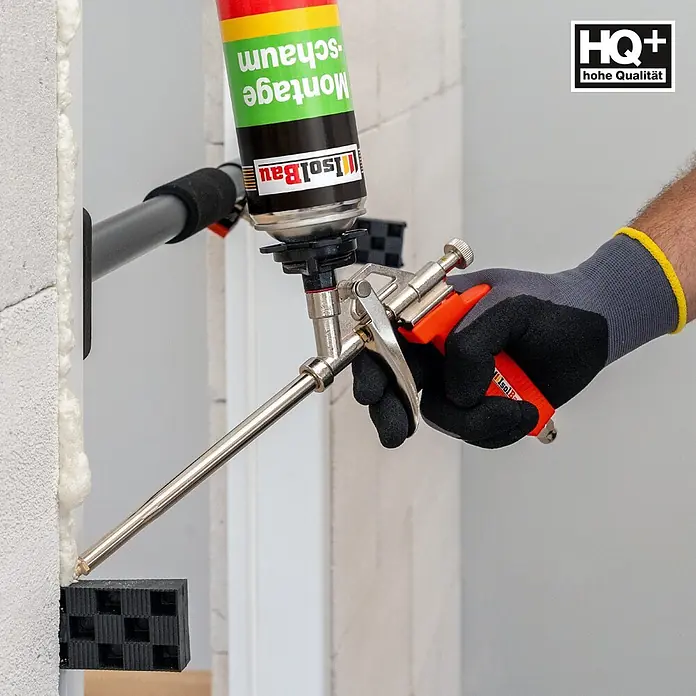 IsolBau Bauschaum 1 x Montageschaum 750 ml - 750 ml - Hand in grauem Handschuh hält Metall-Schaumpistole mit Montageschaumdose, Schaum wird in einen Bauspalt gespritzt.