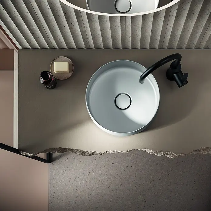Bette Waschtisch - 420 x 420 cm - Draufsicht auf ein hellgraues rundes Waschbecken mit schwarzer Armatur auf einer beigen Ablage.