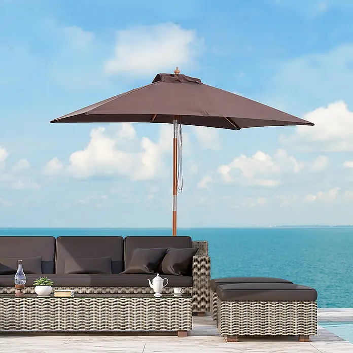 Outsunny Marktschirm - Kaffeebraun - Outdoor-Rattanset mit dunklen Polstern und braunem Sonnenschirm auf einer Terrasse am Meer.