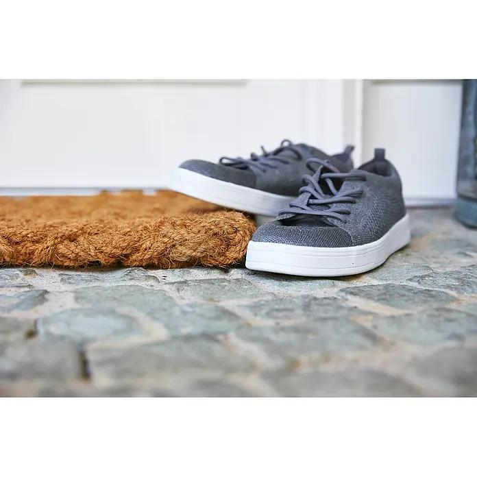 Fußmatte Nature Classic - 75 x 45 cm, Natur, Material Nutzschicht: 100 % Kokos, Karo - Paar graue Stoff-Sneaker mit weißen Sohlen auf einer Kokosfußmatte auf Kopfsteinpflaster.