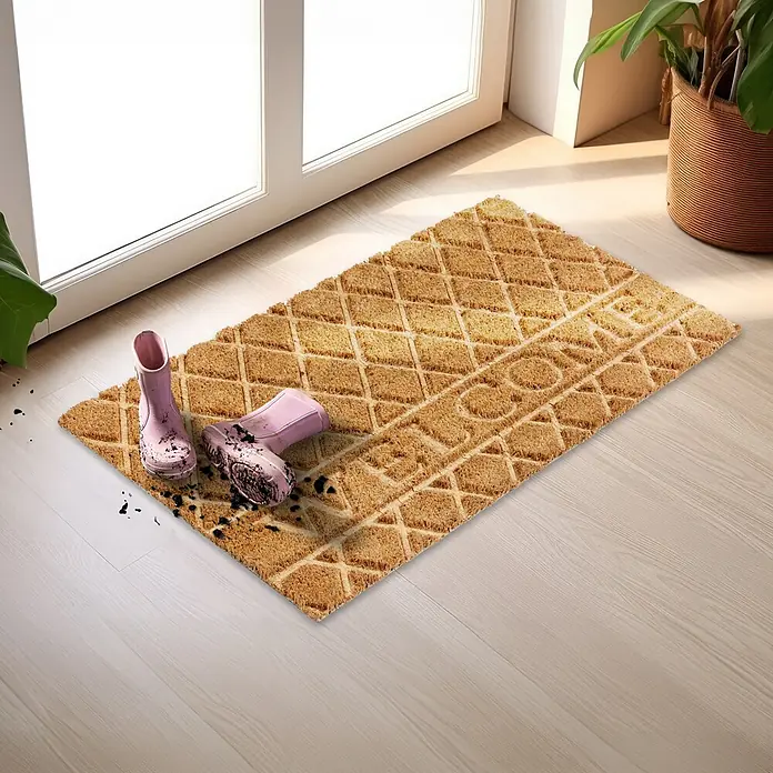Fußmatte Coco Shape - 75 x 45 cm, Natur, Material Nutzschicht: 100 % Kokos, Welcome - Natürliche Kokos-Fußmatte mit Rautenmuster und „WELCOME“-Schriftzug, mit schlammigen rosa Stiefeln am Eingang.