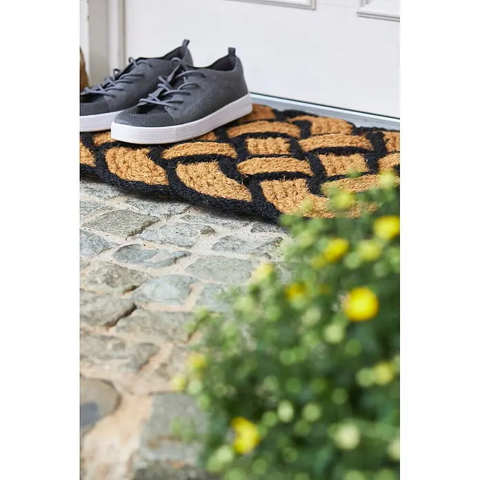 Fußmatte Nature Classic - 75 x 45 cm, Natur/Schwarz, Material Nutzschicht: 100 % Kokos - Natur-Kokosfußmatte mit schwarzem geometrischem Muster, darauf ruhen graue Sneaker vor einer Tür.