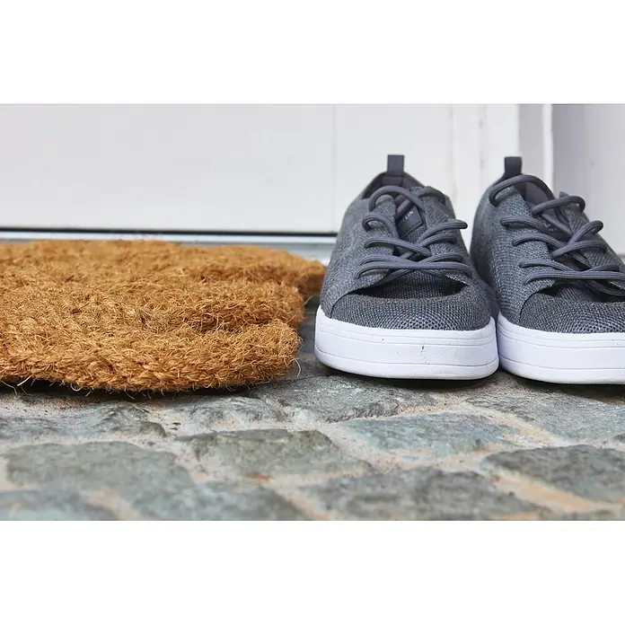 Fußmatte Nature Classic - 75 x 45 cm, Natur, Material Nutzschicht: 100 % Kokos - Eine Kokos-Fußmatte neben einem Paar grauer gewebter Sneaker mit weißen Sohlen auf Steinboden.
