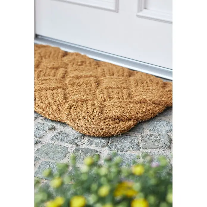 Fußmatte Nature Classic - 75 x 45 cm, Natur, Material Nutzschicht: 100 % Kokos - Naturbraune Kokosfasermatte mit Webmuster, vor einer weißen Tür auf einer Steinterrasse platziert.