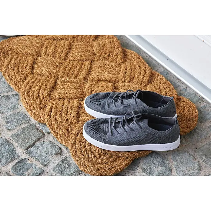 Fußmatte Nature Classic - 75 x 45 cm, Natur, Material Nutzschicht: 100 % Kokos - Ein Paar graue Strick-Sneaker mit weißen Sohlen liegt auf einer geflochtenen Kokos-Fußmatte am Eingang.