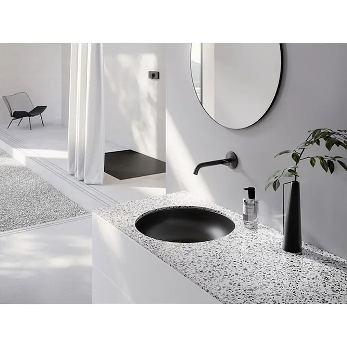 Bette Unterbauwaschbecken -  - Schwarzes rundes Waschbecken, integriert in eine gesprenkelte Arbeitsplatte mit schwarzem Wandhahn, in einem modernen Badezimmer.