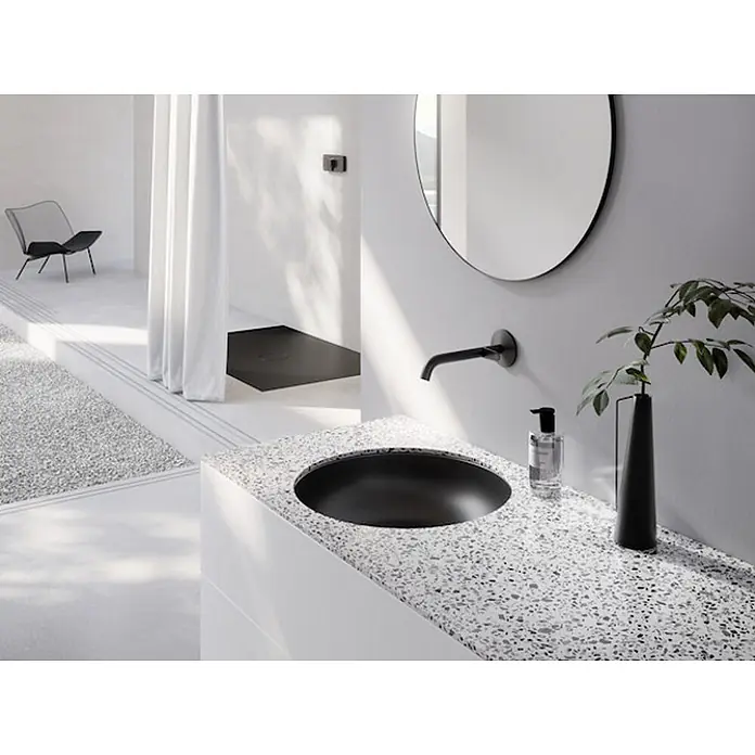 Bette Unterbauwaschbecken -  - Modernes Badezimmer mit schwarzem Waschbecken in einer weißen Terrazzo-Arbeitsplatte, wandmontierter Armatur und rundem Spiegel.