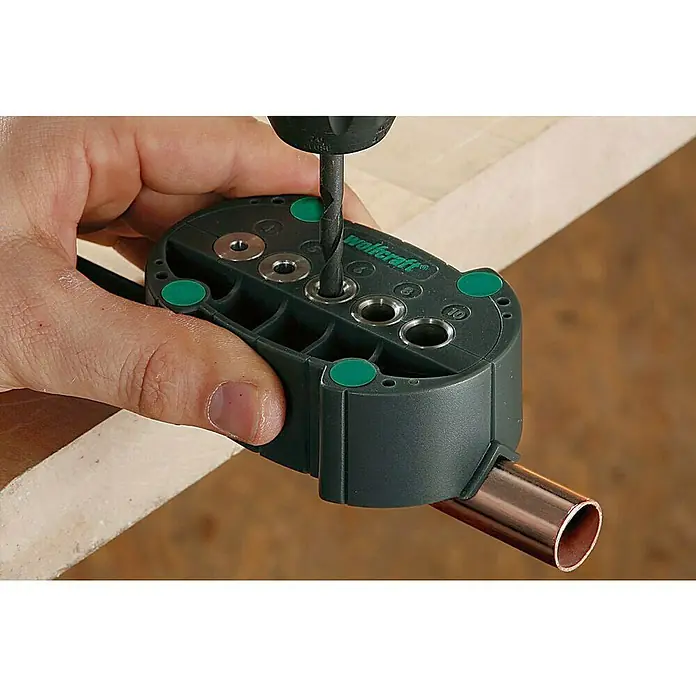 Wolfcraft Guía para taladrar - Diámetro: 4 mm - 10 mm - La imagen muestra una guía de taladro Wolfcraft en acción, utilizada para perforar con precisión en piezas de trabajo, con un tubo de cobre insertado.