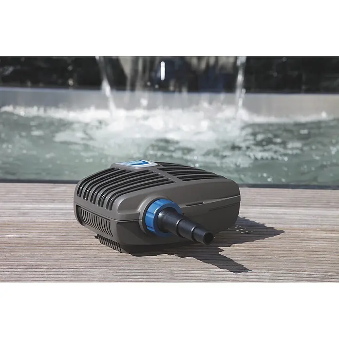 Oase Filterpumpe Aqua Max Eco Classic 2500 E - 23 W, Fördermenge pro Std.: 2.600 l - Grauer Teichfilter mit blauem Anschlussstück auf Holzterrasse, im Hintergrund ein unscharfer Brunnen.
