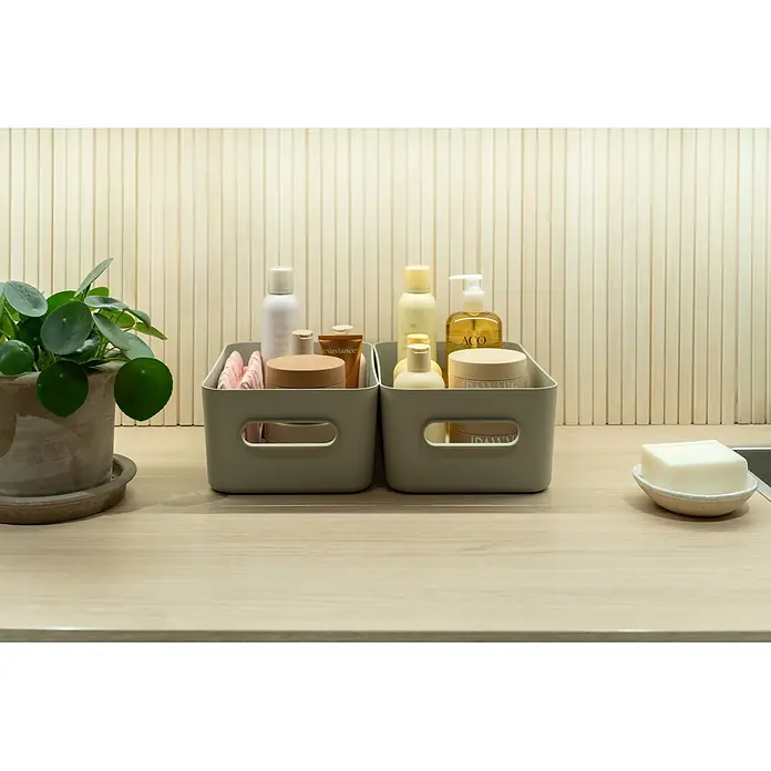 SmartStore Aufbewahrungsbox Comfort M - L x B x H: 29,5 x 19,5 x 12 cm, Kunststoff, Moss, 5,3 l - Zwei graue Aufbewahrungsboxen mit verschiedenen Toilettenartikeln auf einer Holztheke.