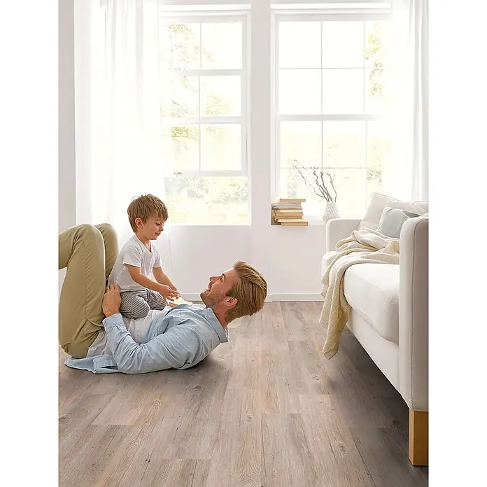 Decolife Designboden Freestyle Access Kenai Oak - 1.220 x 185 x 8,5 mm, Landhausdiele, Kenai Oak - Heller Holzboden mit spielendem Vater und Kind, der die einladende Atmosphäre im hellen Wohnzimmer hervorhebt.