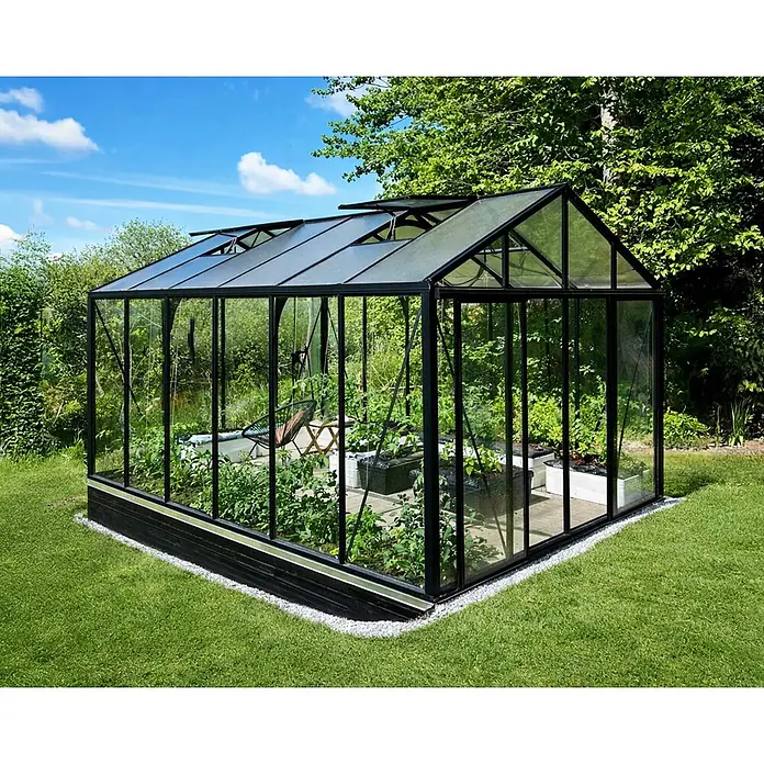 Bloomcabin Gewächshaus Aluminium Klassik - Außenmaß inkl. Dachüberstand (B x T): 309 x 459 cm, Material Seitenwand: Glas, 4 mm, Schwarz - Großes schwarzgerahmtes Gewächshaus mit klaren Scheiben, gefüllt mit Pflanzen und Sitzbereich, in einem Außenbereich aufgestellt.