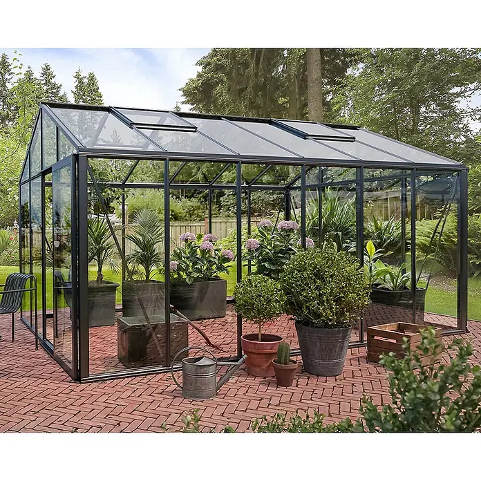Bloomcabin Gewächshaus Aluminium Klassik - Außenmaß inkl. Dachüberstand (B x T): 309 x 459 cm, Material Seitenwand: Glas, 4 mm, Schwarz - Großes Gewächshaus mit schwarzem Rahmen und Glas, mit Pflanzen innen und außen, auf einer roten Backsteinterrasse.