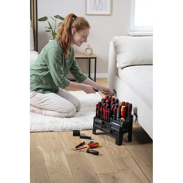 Alpha Tools Set de destornilladores - 101 pzs. - Gran juego de destornilladores y puntas negro y rojo utilizado por una mujer arreglando un sofá.