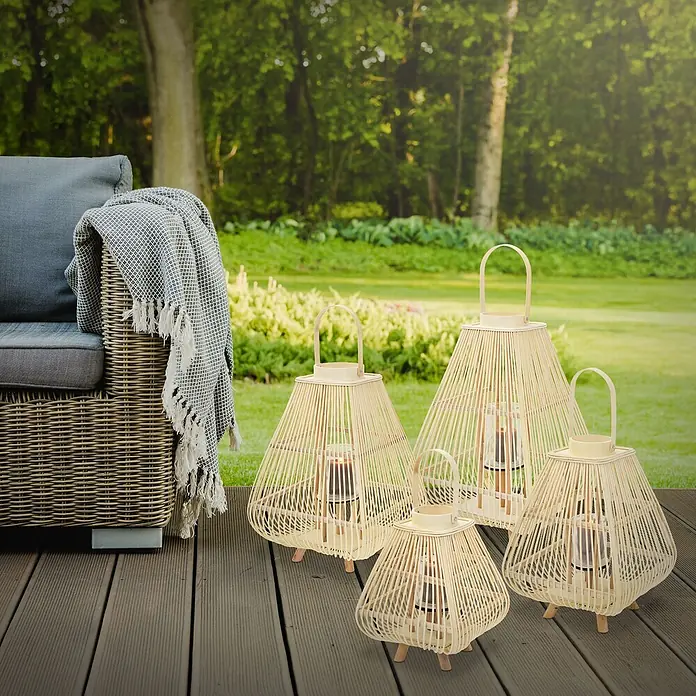 ECD Germany Windlicht Boho Bambus Laterne - Natur, 1 Stk. - Vier unterschiedlich große Laternen aus hellem Bambus mit Kerzenlicht auf einer Holzterrasse neben einem Sofa.