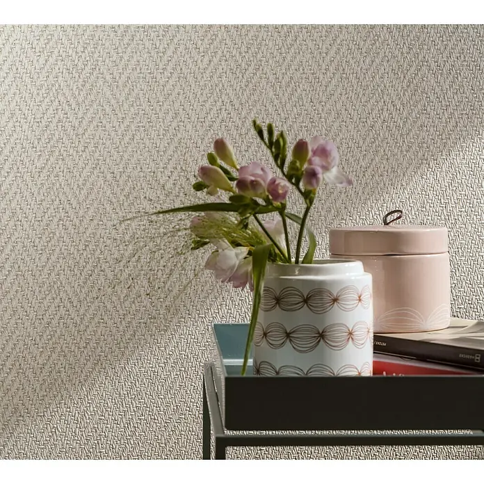 Marburg Loft Vliestapete Fischgrät-Textilstruktur - Hellbraun, Grafisch, 10,05 x 0,53 m - Nahaufnahme eines strukturierten Hintergrunds mit Blumen, einer Dose und einem Buch auf einem Tablett, das eine warme und gemütliche Atmosphäre schafft.