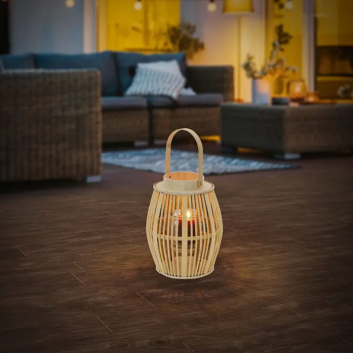 ECD Germany Windlicht Boho Bambus Laterne - Ø x H: 23 x 30 cm, Natur, 1 Stk. - Eine helle Bambuslaterne mit roter Kerze steht auf dunklem Holzboden und taucht eine Terrasse in warmes Licht.