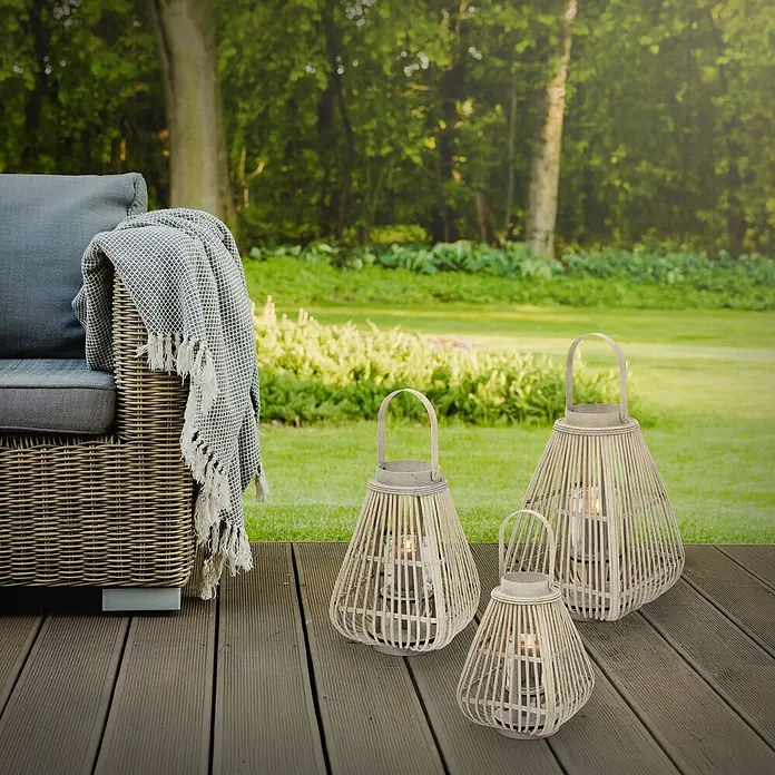 ECD Germany Windlicht Boho Bambus Laterne - Ø x H: 24 x 50 cm, Natur, 1 Stk. - Drei Bambuslaternen mit brennenden Kerzen auf einer Holzterrasse neben einem Outdoor-Sofa.
