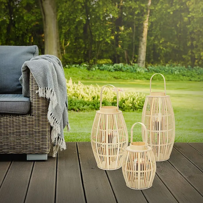 ECD Germany Windlicht Boho Bambus Laterne - Ø x H: 30 x 75 cm, Natur, 1 Stk. - Drei Bambuslaternen in verschiedenen Größen mit brennenden Kerzen auf einer Holzterrasse neben einem Outdoor-Sofa.