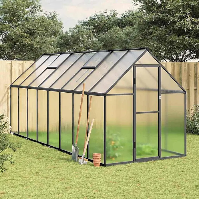 Furnicato Gewächshaus - 169 x 445 cm, Material Seitenwand: Kunststoff, 38 mm, anthrazit - Schwarz gerahmtes Gewächshaus mit durchscheinenden Platten in einem Garten, Gartenwerkzeuge lehnen daran.