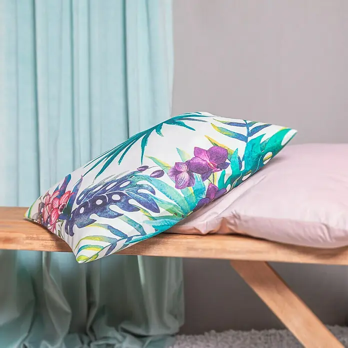 Expo Ambiente Schlaufenbandschal Samtschal Velvet - 135 x 245 cm, 100 % Polyester, Hellgrün - Nahaufnahme eines Kissens mit tropischem Blumenmuster auf einer Holzbank, das eine gemütliche und entspannende Atmosphäre schafft.
