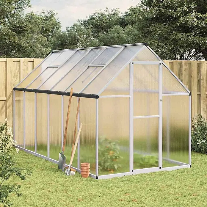 Furnicato Gewächshaus Polycarbonat - 169 x 334 cm, Material Seitenwand: Kunststoff, 38 mm, silbern - Ein geräumiges Gewächshaus mit silbernem Aluminiumrahmen und transparenten Polycarbonatplatten, in einem Garten mit Werkzeugen.