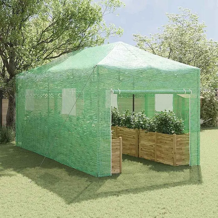 Furnicato Gewächshaus - Außenmaß inkl. Dachüberstand (B x T): 580 x 290 cm, Material Seitenwand: Kunststoff, 38 mm, Grün - Grünes Maschengewächshaus im Garten mit hölzernen Hochbeeten voller Pflanzen.