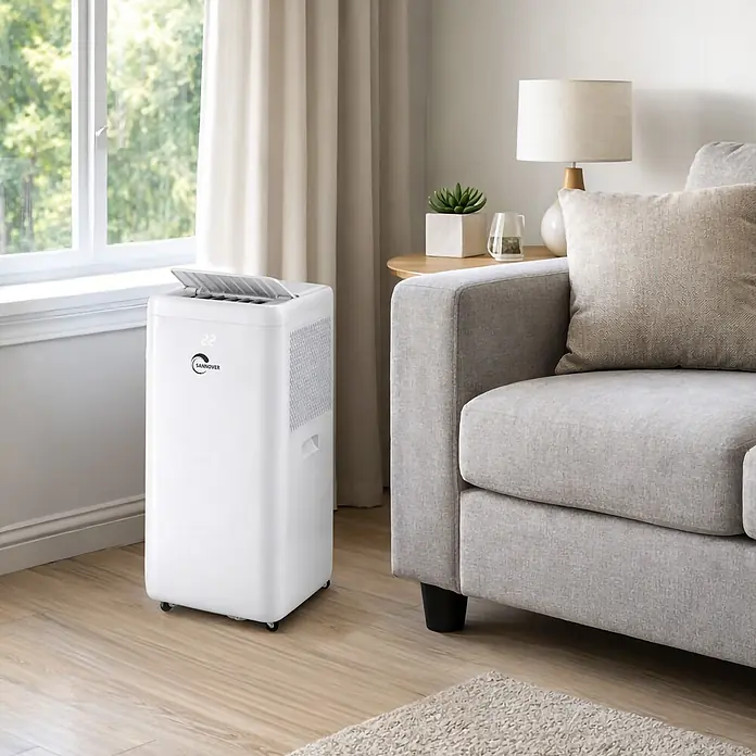 Sannover Mobiles Klimagerät Umkehrbare (Warm/Kalt) 3,5 kW / 12000 BTU Fresho - 3,5 kW, Raumgröße: 35 m², weiß - Weißes, mobiles Klimagerät mit Digitalanzeige und Rollen, in einem modernen Wohnzimmer neben einem Fenster und einem grauen Sofa.