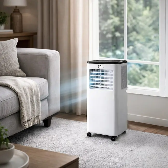 Sannover Mobiles Klimagerät Umkehrbare (Warm/Kalt) 2,9 kW / 10000 BTU Fresho - 2,9 kW, Raumgröße: 16 m², weiß - Weißes tragbares Klimagerät mit schwarzer Oberseite, das blauen Luftstrom in einem Wohnzimmer neben Sofa und Fenster abgibt.
