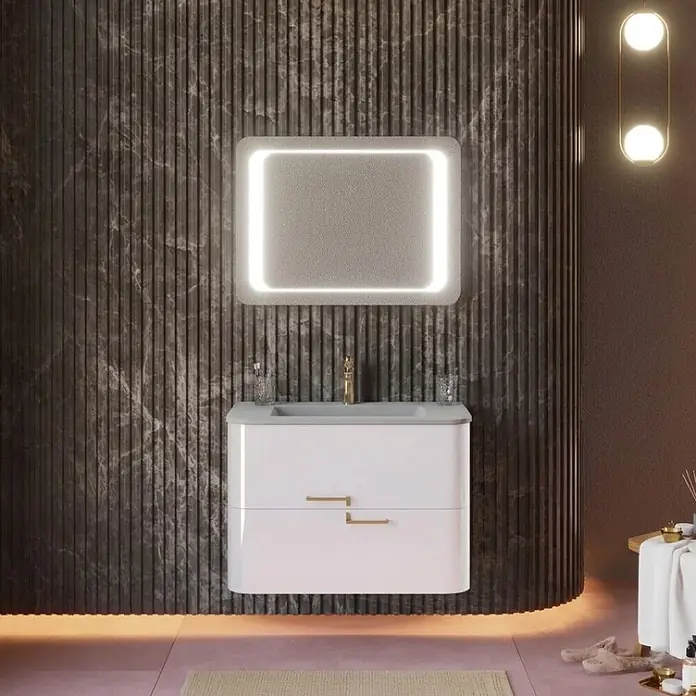 Kiamami Valentina Badmöbel-Set - Weiß - Weißer Badezimmer-Waschtisch mit grauem Waschbecken, goldenem Wasserhahn und rechteckigem, hinterleuchtetem Spiegel vor dunkler, geriffelter Wand.