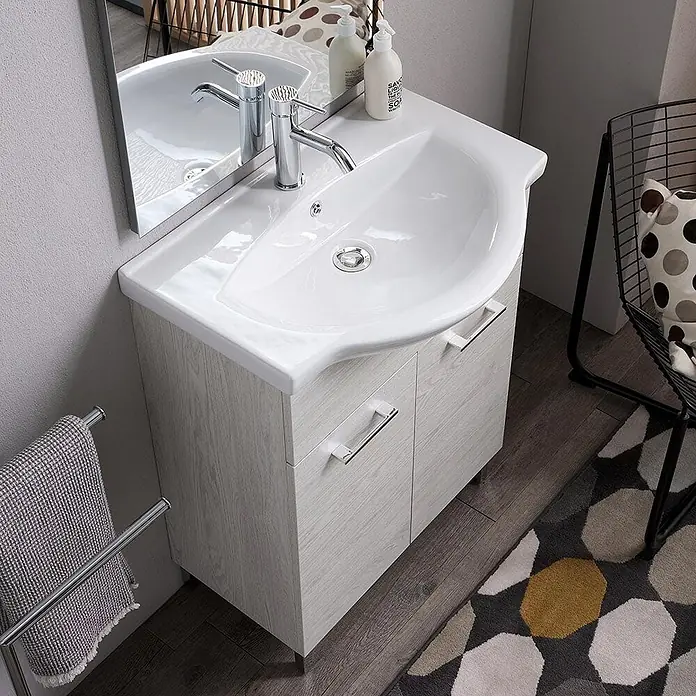 Kiamami Valentina Badmöbel-Set - Helles Holz - Weißes Keramik-Waschbecken mit hellgrauem Holzmaserung-Waschtischunterschrank und Chromarmaturen im Badezimmer.