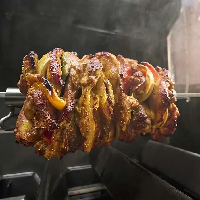 Weber Barbacoa de gas Spirit EPX-435R + Rustidor - Superficie de la parrilla (An x Pr): 61 x 45 cm, 10,3 kW, Número de quemadores: 4 - Carne marinada dorada y verduras (cebollas, pimientos) cocinándose en un asador giratorio de metal, con vapor.