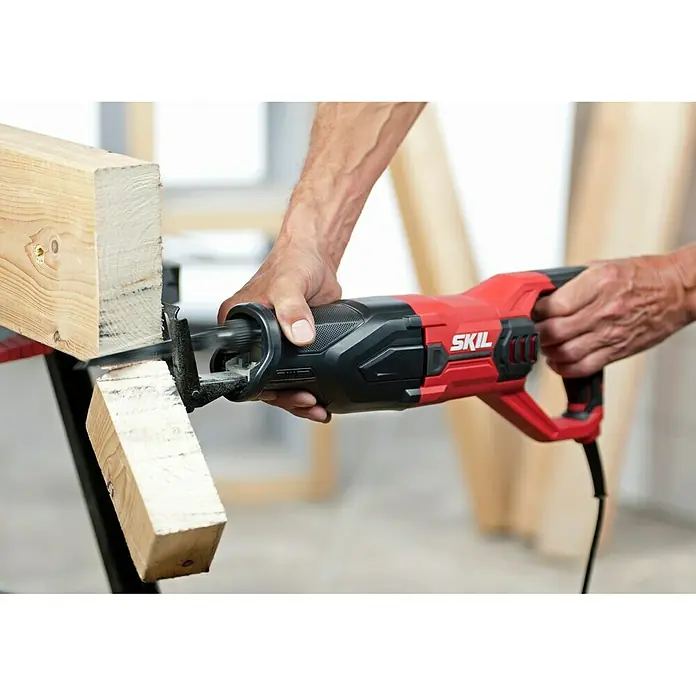 Skil Säbelsäge 4961 AA - 900 W, Hublänge: 29 mm - Das SKIL Säbelsäge-Werkzeug schneidet präzise durch ein Holzstück, gehalten von einer Person, mit dem Fokus auf das rote und schwarze Design der Säge.