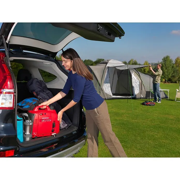 Honda Stromerzeuger EU 10i - Nennleistung: 1,1 kW, Tankvolumen: 2,1 l - Roter Honda EU10i Generator wird aus dem Kofferraum eines Autos auf einem Campingplatz entladen.