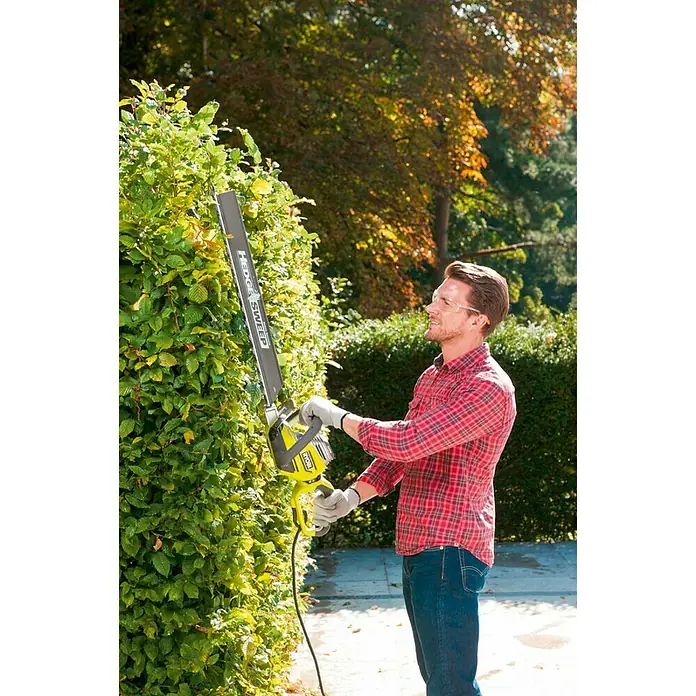 Ryobi Cortasetos eléctrico RHT 8165 RL - 800 W, Longitud de corte: 65 cm - Hombre cortando un seto con un cortasetos RYOBI. El cortasetos RYOBI tiene una hoja extra larga para setos altos.
