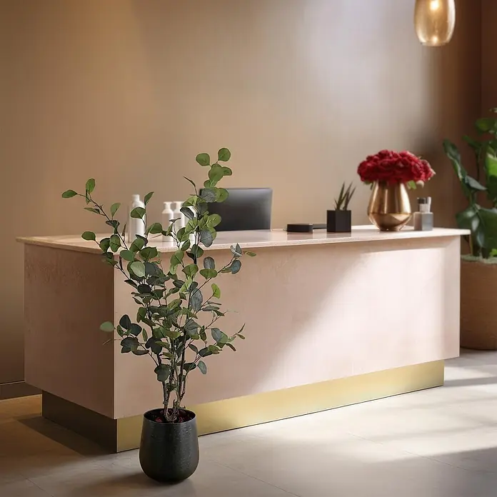 Florora Kunstpflanze Blauer Gummibaum - Höhe: 120 cm, Holz - Hellerrosa Empfangstheke mit goldener Basis, in einem modernen Interieur mit dezenten Dekoelementen.