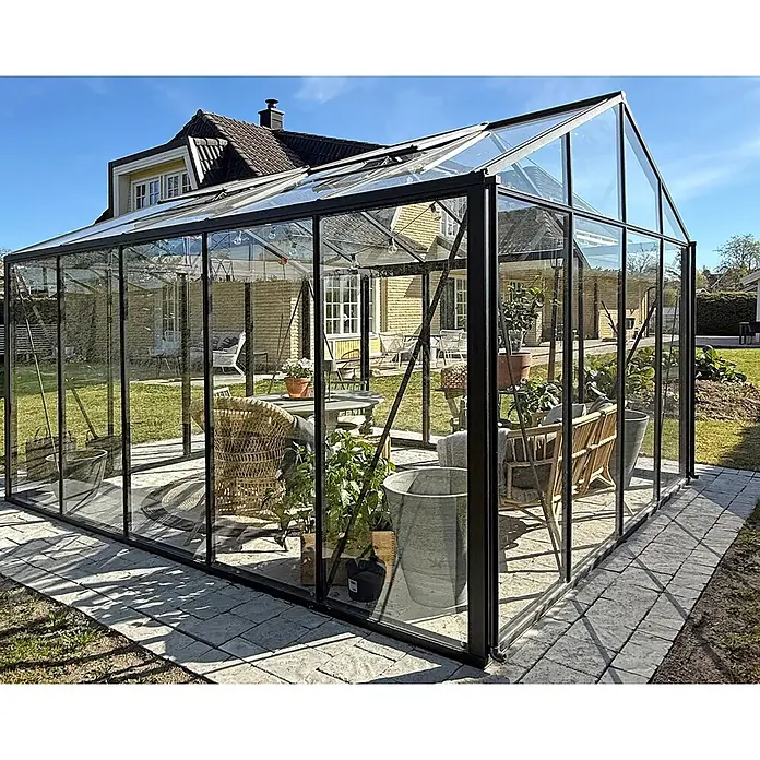 Bloomcabin Gewächshaus Aluminium Klassik - Außenmaß inkl. Dachüberstand (B x T): 309 x 384 cm, Material Seitenwand: Glas, 4 mm, Schwarz - Großes schwarzgerahmtes Gewächshaus aus Glas im Garten, als Wintergarten mit Sitzgelegenheiten und Pflanzen genutzt.