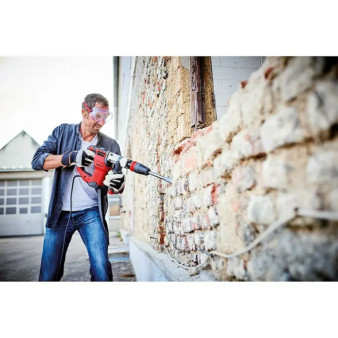 Einhell Abbruchhammer TE-DH 12 - 1.050 W, 12 J, SDS-Max-Aufnahme - Ein Mann benutzt einen Einhell Abbruchhammer, um eine Ziegelwand einzureißen, wobei er Schutzbrille und Handschuhe trägt.