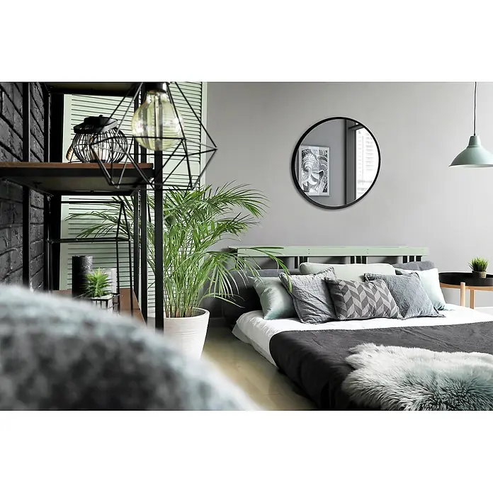 Tulup Wandspiegel - 100 x 100 cm - Modernes Schlafzimmer mit niedrigem Bett, grauer und minzgrüner Bettwäsche, rundem schwarzem Spiegel und großer Topfpflanze. Links ein schwarzes Industrieregal.