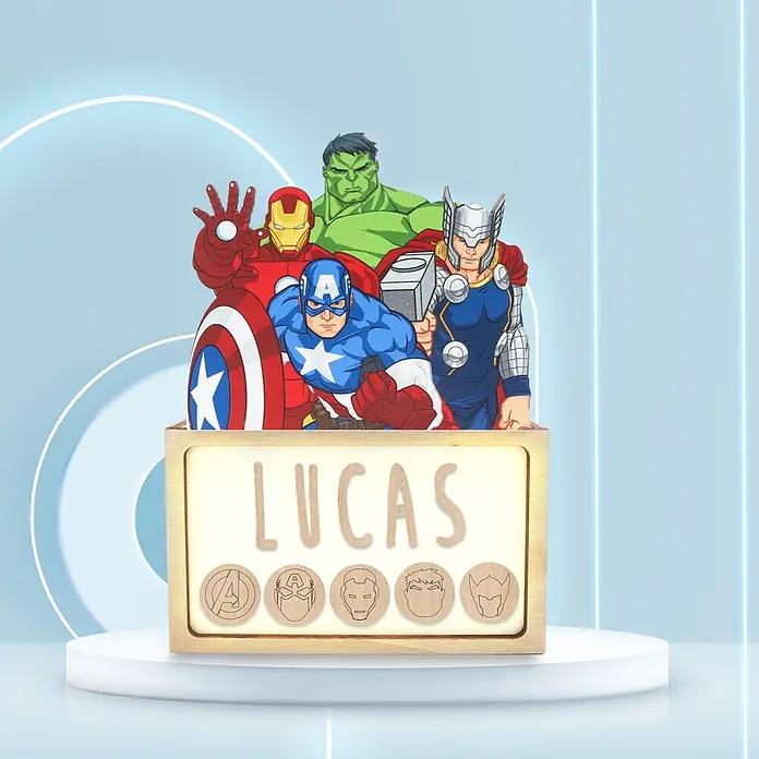 Lámpara de sobremesa infantil Avengers - 0,5 W, L x An x Al: 5 x 12,5 x 17 cm, Luz nocturna, Avengers - Lámpara de noche Avengers personalizada de madera con nombre "Lucas" y recortes de personajes, en un podio blanco sobre fondo azul.
