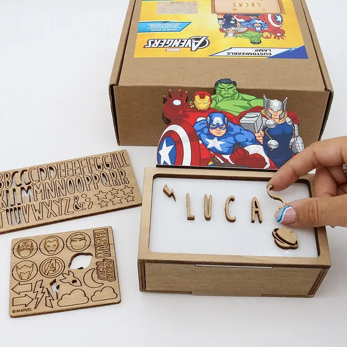 Lámpara de sobremesa infantil Avengers - 0,5 W, L x An x Al: 5 x 12,5 x 17 cm, Luz nocturna, Avengers - Kit de lámpara Avengers personalizable con letras de madera y formas Marvel. Una mano coloca una letra en la caja de luz.