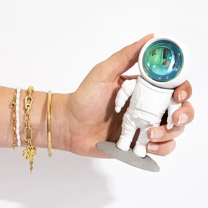 Mob Lámpara de sobremesa LED Astrolight Rainbow - 5 W, L x An x Al: 6,5 x 6 x 12 cm, Blanco, Multicolor, Rainbow - Una mano sostiene una pequeña figura de astronauta blanca con visera iridiscente y una base gris.