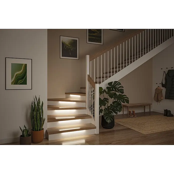 Paulmann MaxLED LED-Stripes Treppenlicht - Länge: 0,5 m, Warmweiß, 1 Stk. - Beleuchtete Holztreppe in einem modernen Flur mit Zierpflanzen und gerahmter Kunst.